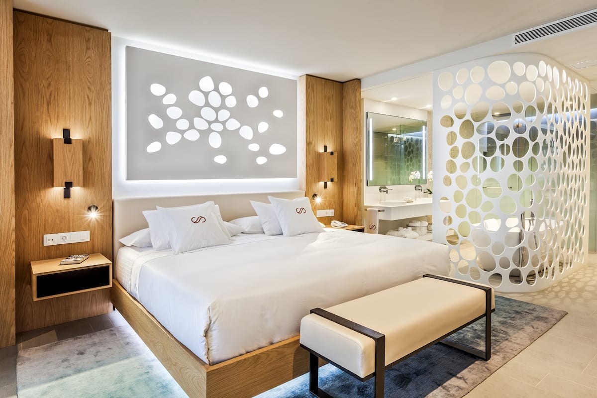 A modern bedroom with a large bed, bedside tables, a bench, and a decorative wall panel.