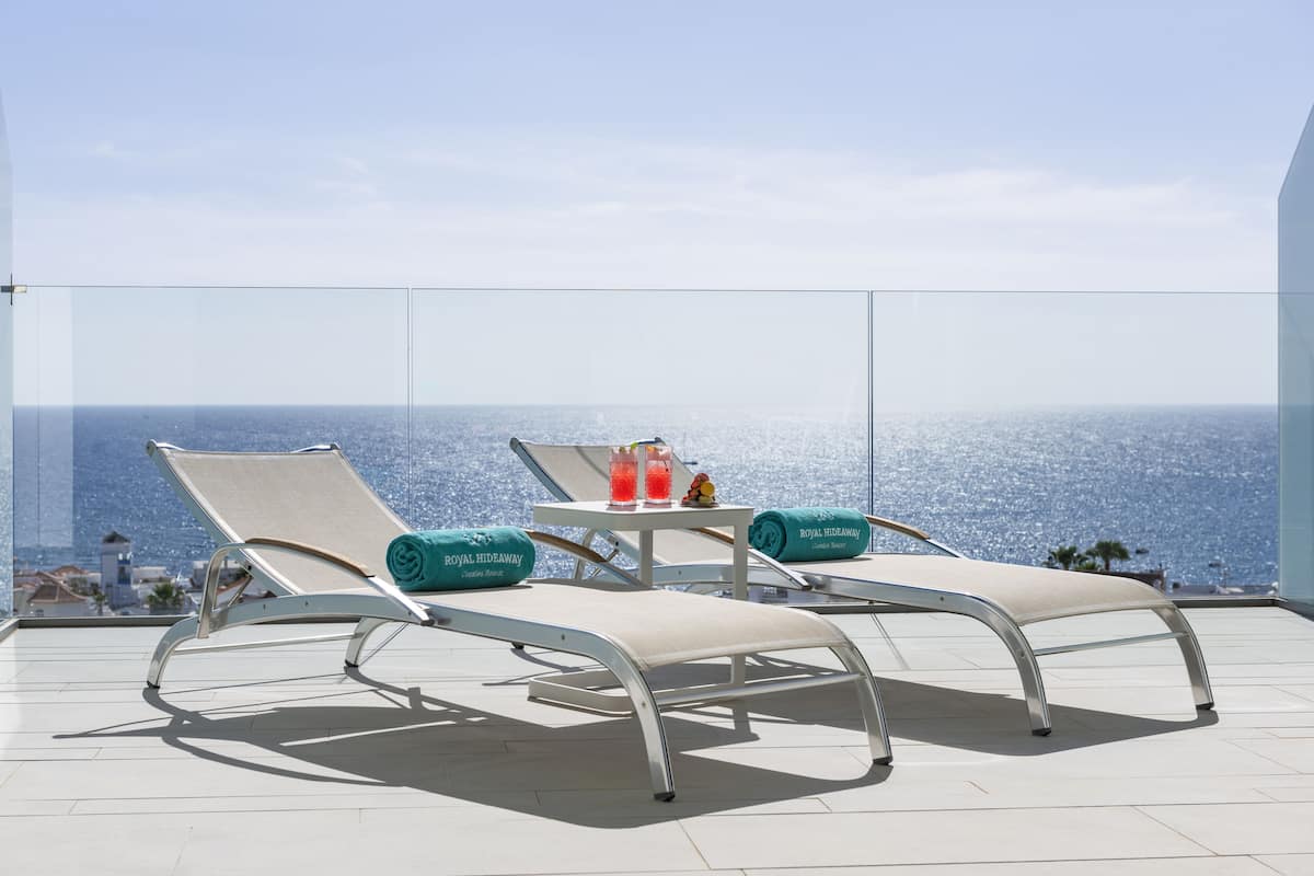 A balcony with two lounge chairs, a small table with drinks, and a view of the ocean.