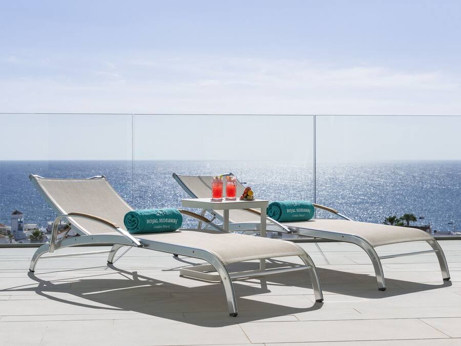 Un balcón con dos sillones, una mesita con bebidas y vista al océano.