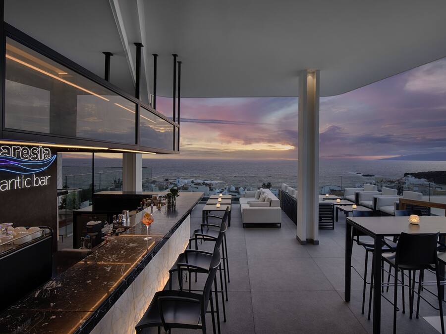 Un bar en la azotea con vistas a la ciudad y al mar al atardecer.