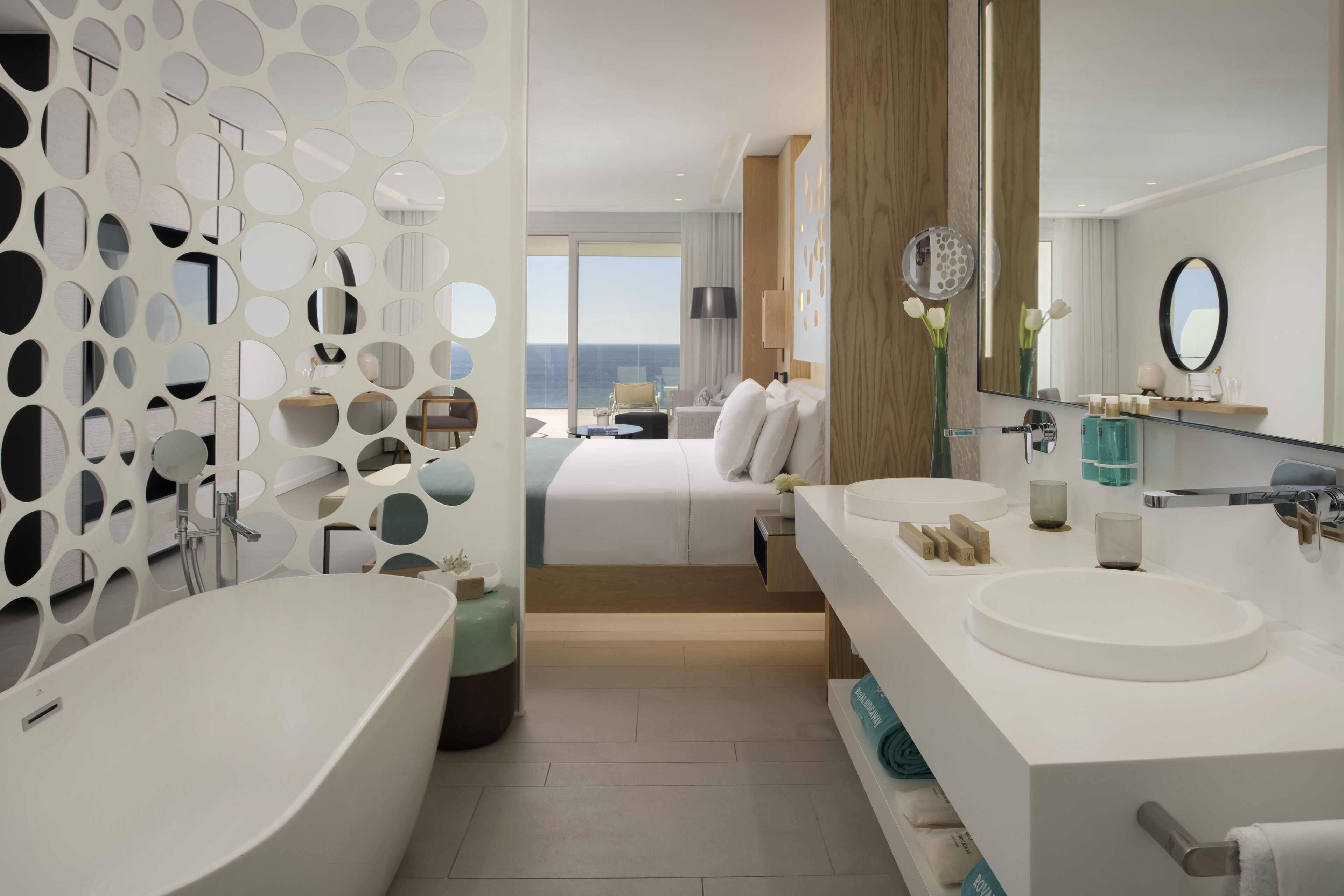 A modern hotel bathroom with a large bathtub, a round sink, and a mirror.