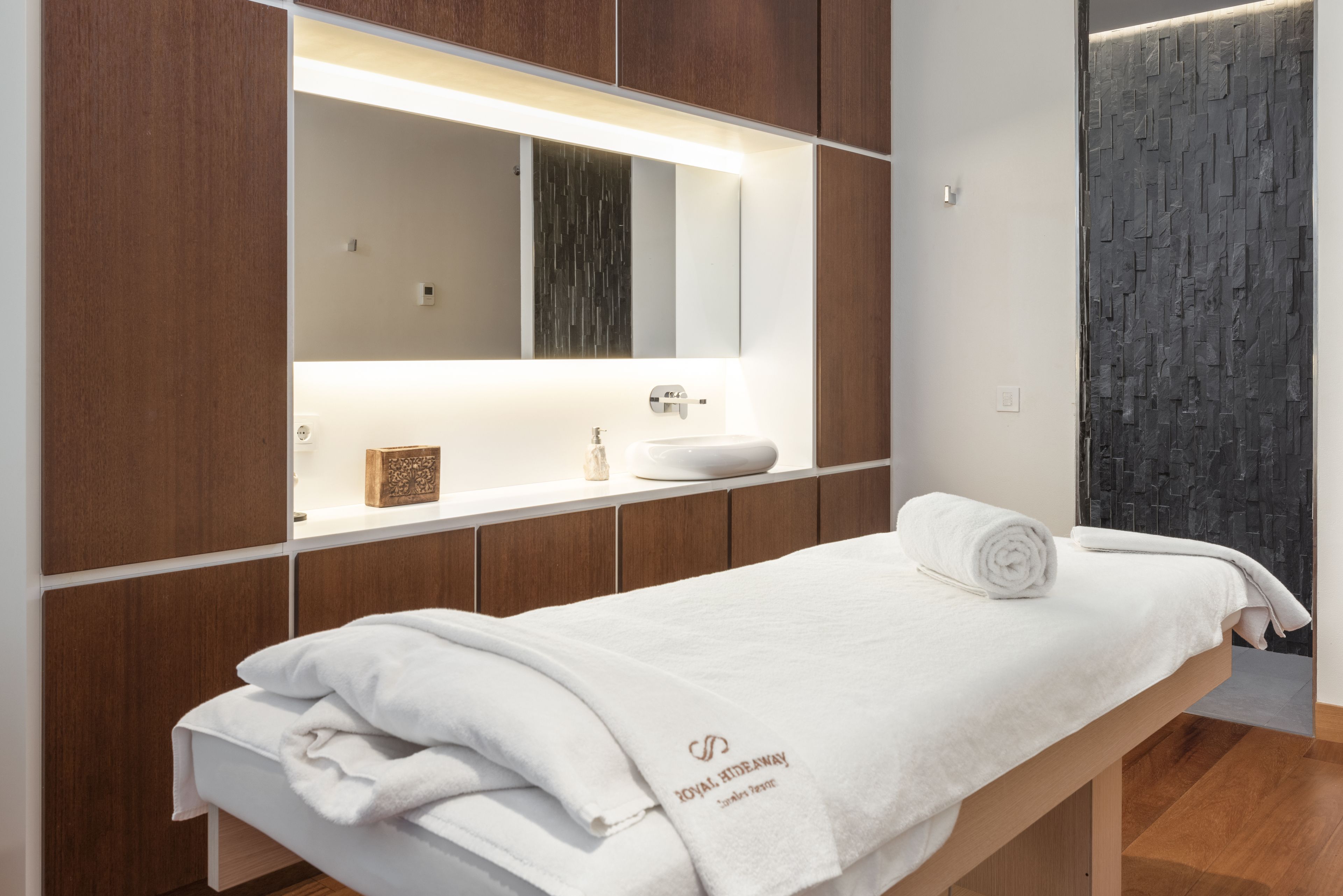A modern bathroom with a wooden vanity, a large mirror, and a white towel on a bench.