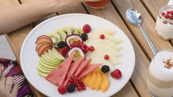 A wooden table with a plate of fruit, a glass of smoothie, and a dessert.