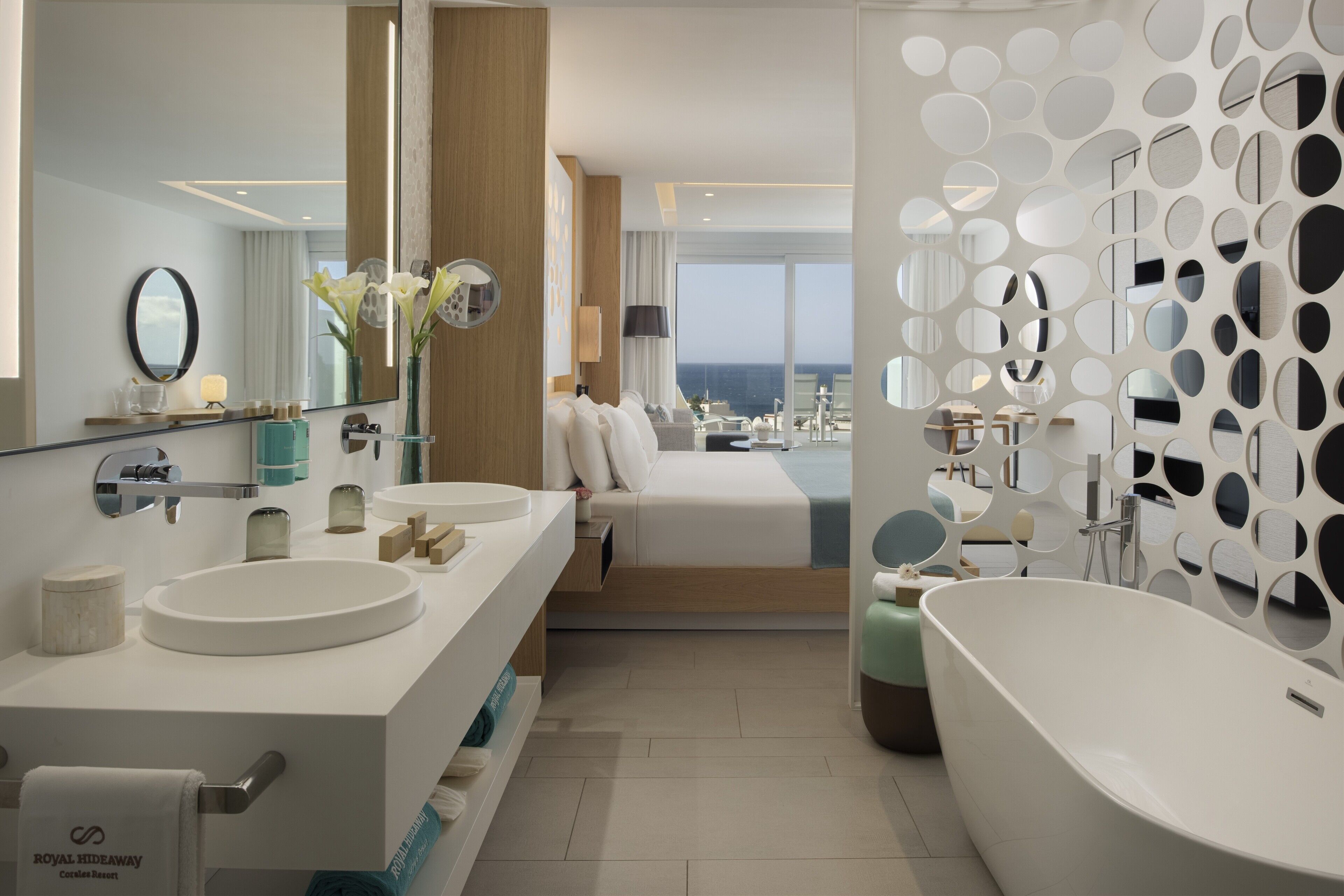 A modern hotel bathroom with dual sinks, a large bathtub, and a view of the ocean.