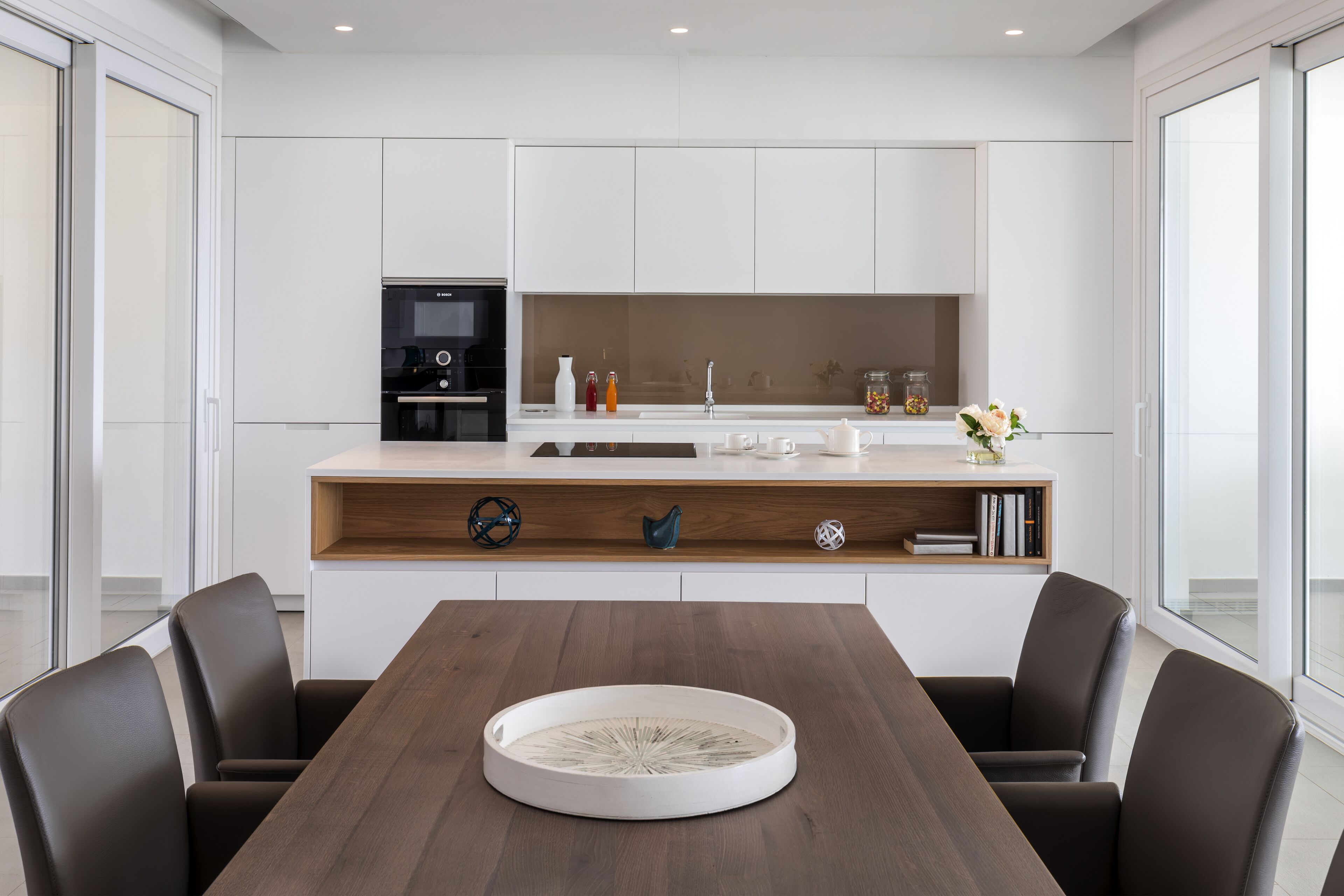 Una cocina moderna con armarios blancos, una mesa de comedor de madera y dos sillas.