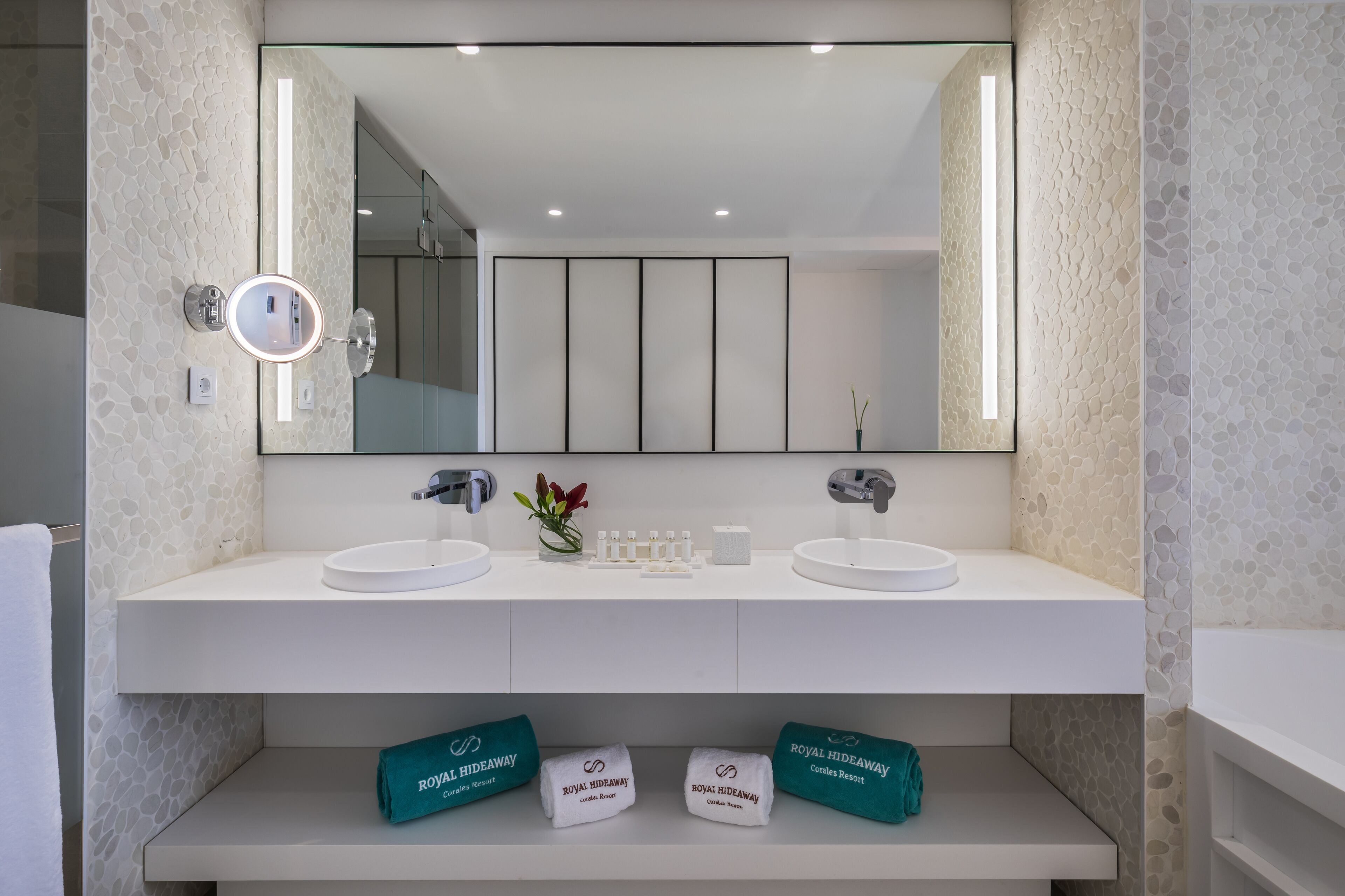 A modern bathroom with two sinks, a large mirror, and a shelf with towels labeled "Royal Hideaway."