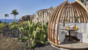 A circular wooden structure with a table and seating, surrounded by cacti and a rocky cliff. - Royal Hideaway Corales Suites, part of Barceló Hotel Group (Adeje)