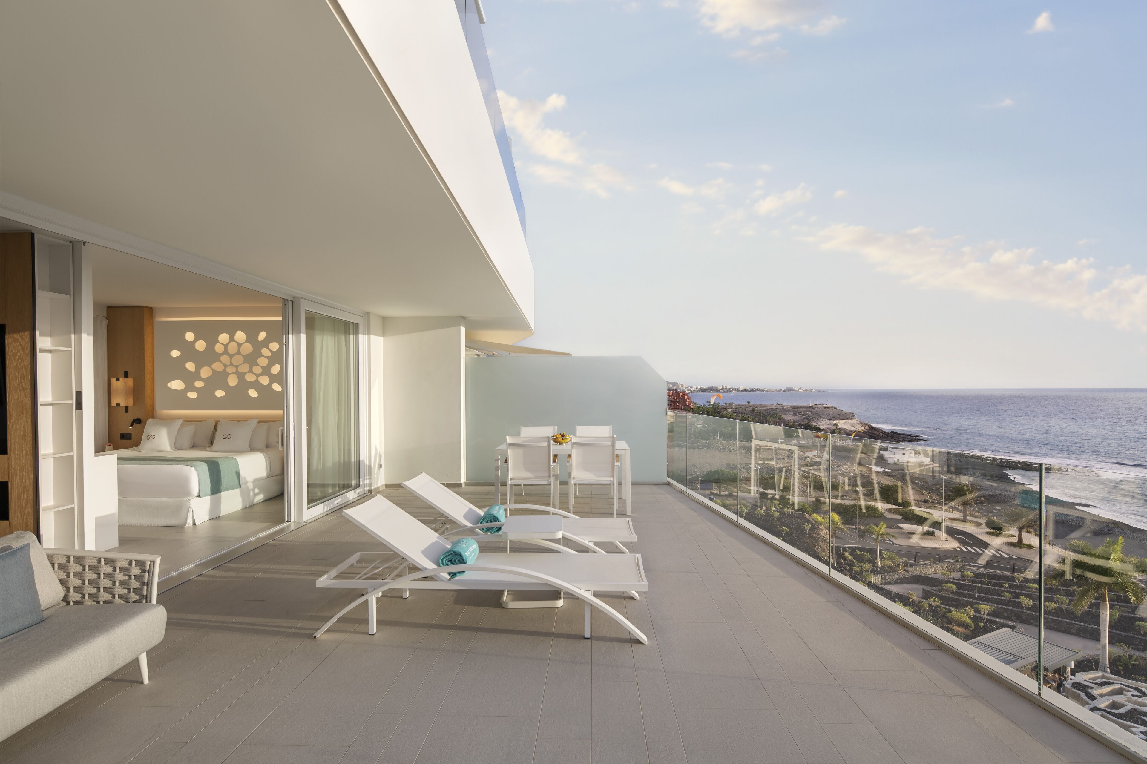 A modern balcony with white furniture, a view of the ocean, and a glass railing.