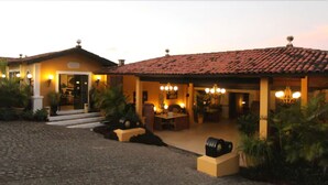 A two-story building with a tiled roof, a front porch with seating, and a driveway leading to the entrance.