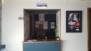 Un comptoir d’accueil avec un panneau d’affichage, des photos encadrées et un calendrier.