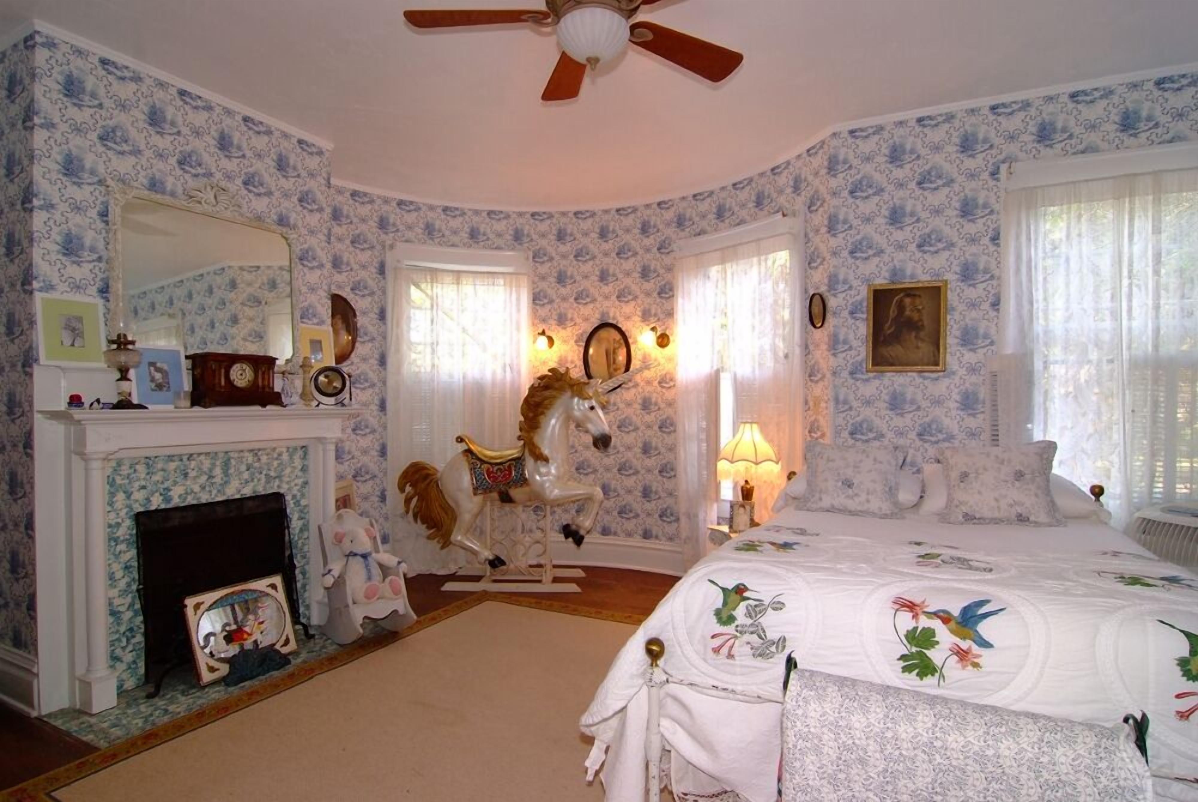 Un dormitorio con chimenea, una cama con ropa de cama floral, un carrusel de caballos y un ventilador de techo.