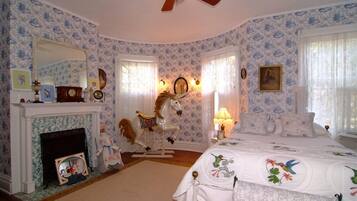 Un dormitorio con chimenea, una cama con ropa de cama floral, un carrusel de caballos y un ventilador de techo.