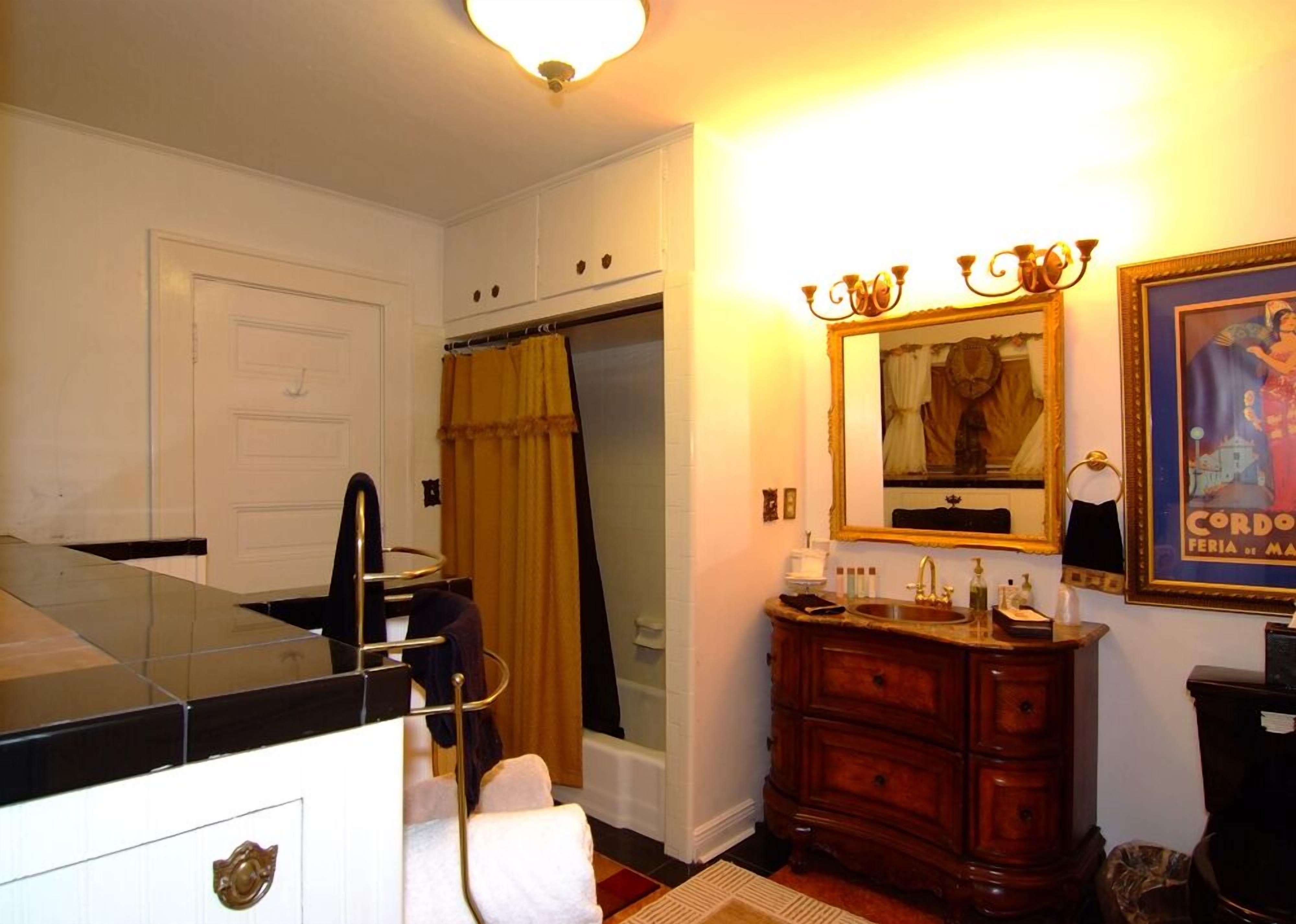 A bathroom with a shower, a vanity with a mirror, and a framed picture on the wall.