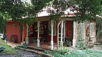 Un edificio rústico con un porche, rodeado de vegetación y un jardín.