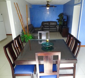 A dining area with a rectangular table, blue cushioned chairs, and a ceiling fan. - Jaco Beach Condos (Jacó)