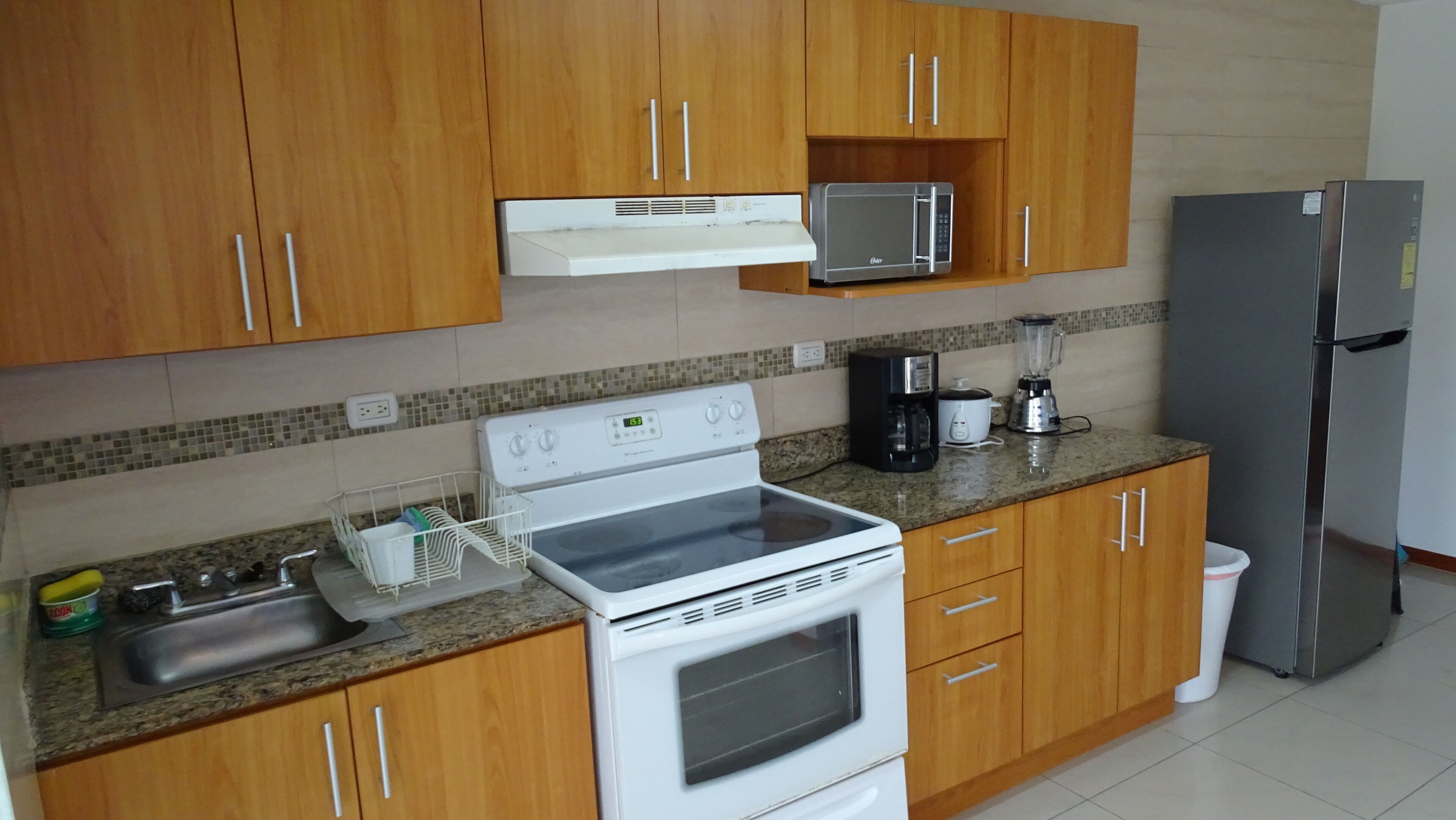 A kitchen with wooden cabinets, a microwave, a refrigerator, a stove, and a coffee maker.