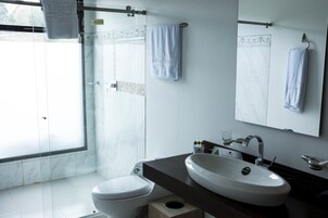 Un baño moderno con un ventanal grande, un inodoro blanco, un lavamanos y dos toallas colgadas en la pared.