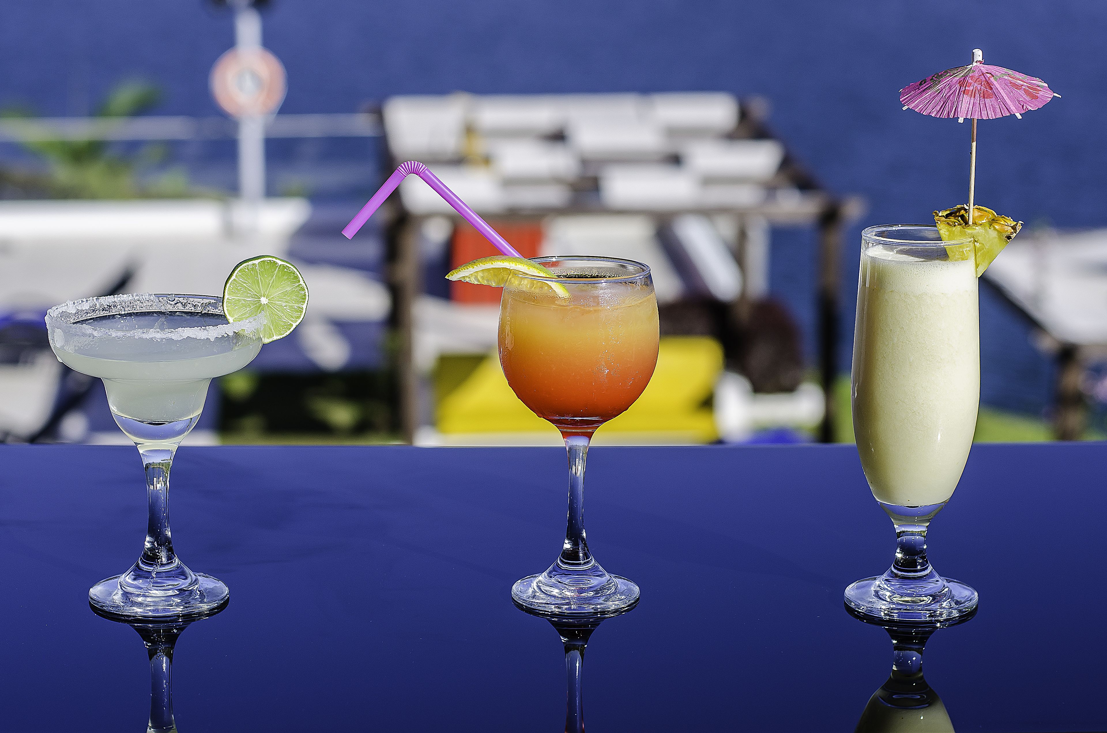 Three cocktails on a table with a blue surface.