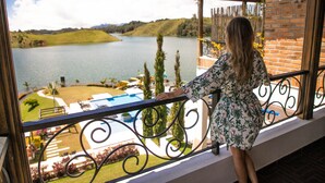 A balcony with a view of a lake, a pool, and surrounding greenery. - Hotel La Magdalena (El Peñol)