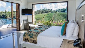 A bedroom with a large window, a bed with patterned bedding, a bedside table with a phone, and a TV on the wall. - Hotel La Magdalena (El Peñol)