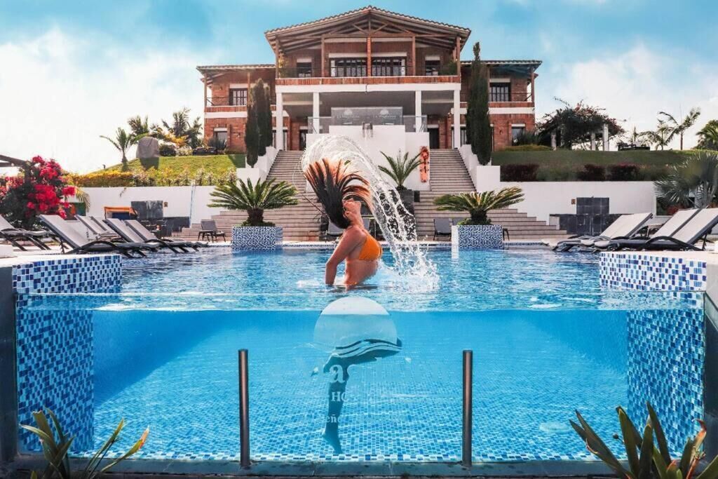 Une piscine avec une personne à l’intérieur, un bâtiment doté d’un toit en tuiles et un escalier menant à ce bâtiment.