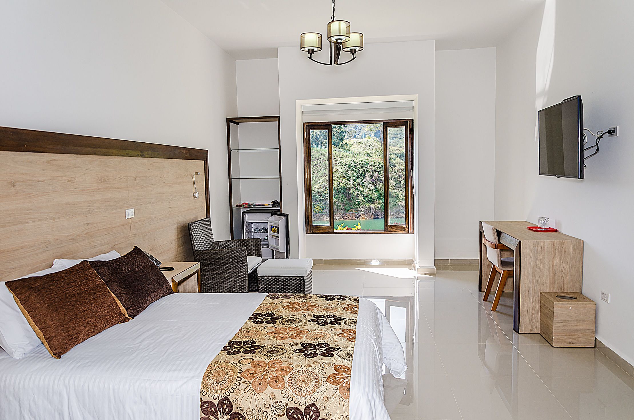 Een hotelkamer met een groot bed, een bureau, een stoel, een aan de muur bevestigde televisie en een raam met uitzicht op groen.