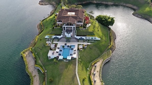 An aerial view of a large, multi-story house with a swimming pool, surrounded by water and greenery. - Hotel La Magdalena (El Peñol)