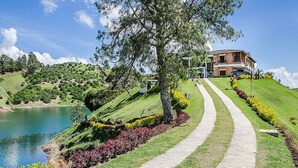 A pathway leading to a building with a brick facade, surrounded by landscaped gardens and a lake. - Hotel La Magdalena (El Peñol)