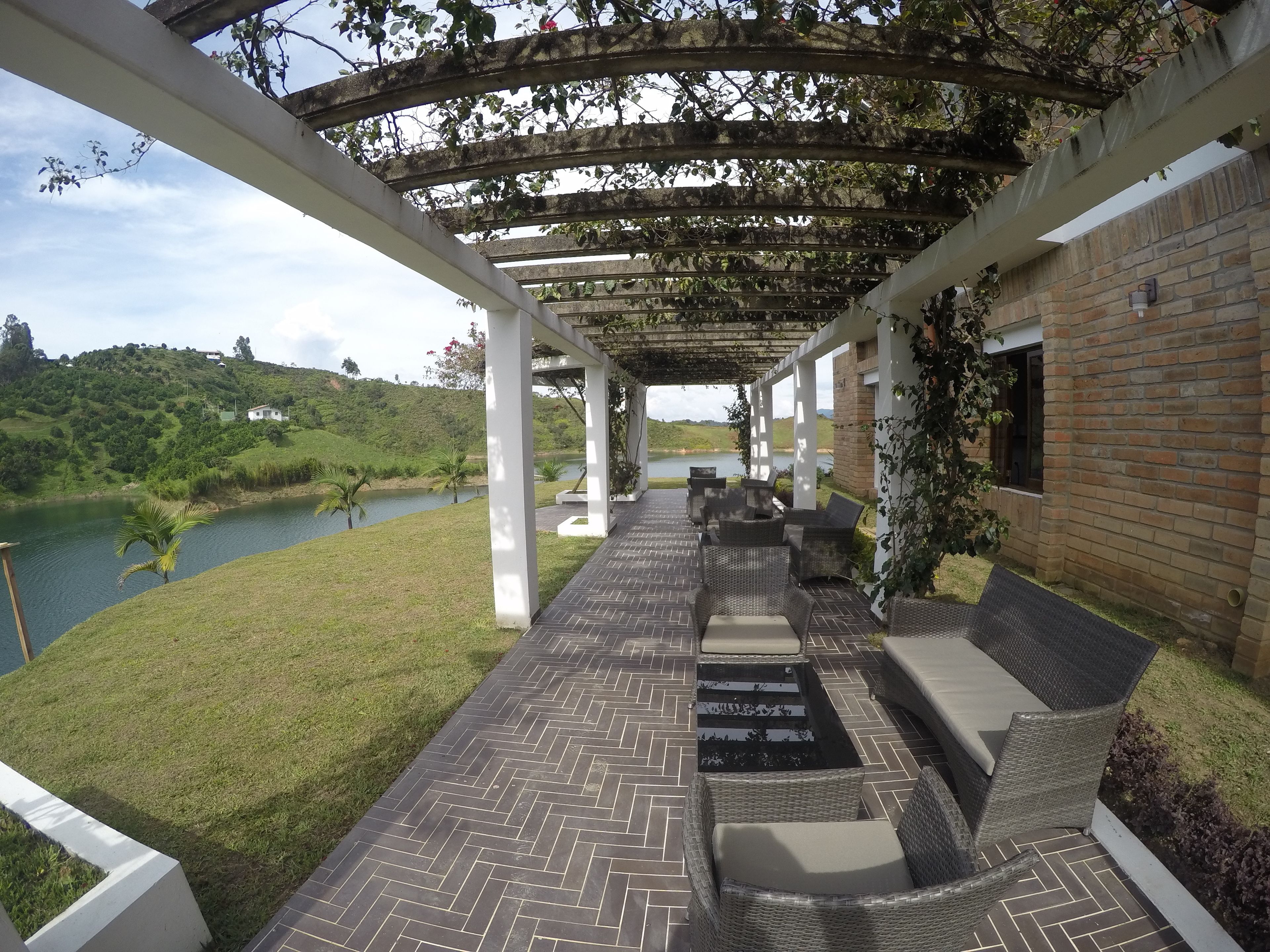 Un espacio de estar al aire libre cubierto con muebles de mimbre y vistas a un lago y colinas.