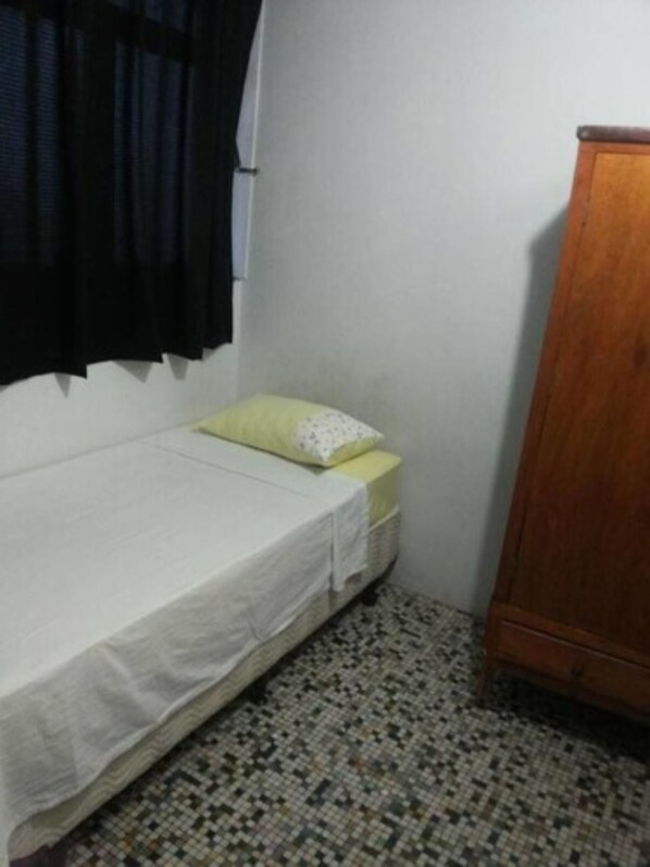 Una habitación pequeña con cama individual, un armario de madera, piso estampado y pared blanca lisa.