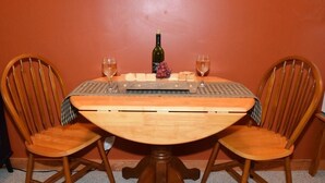 A wooden dining table with a checkered table runner, two wooden chairs, a bottle of wine, a glass of wine, and a plate of cheese and grapes. - Beagle's Bed & Breakfast (Paxinos)