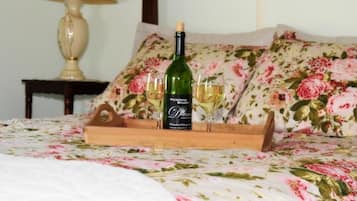 A bed with a floral bedspread, a bottle of Pickering Dream wine, and two glasses on a wooden tray.