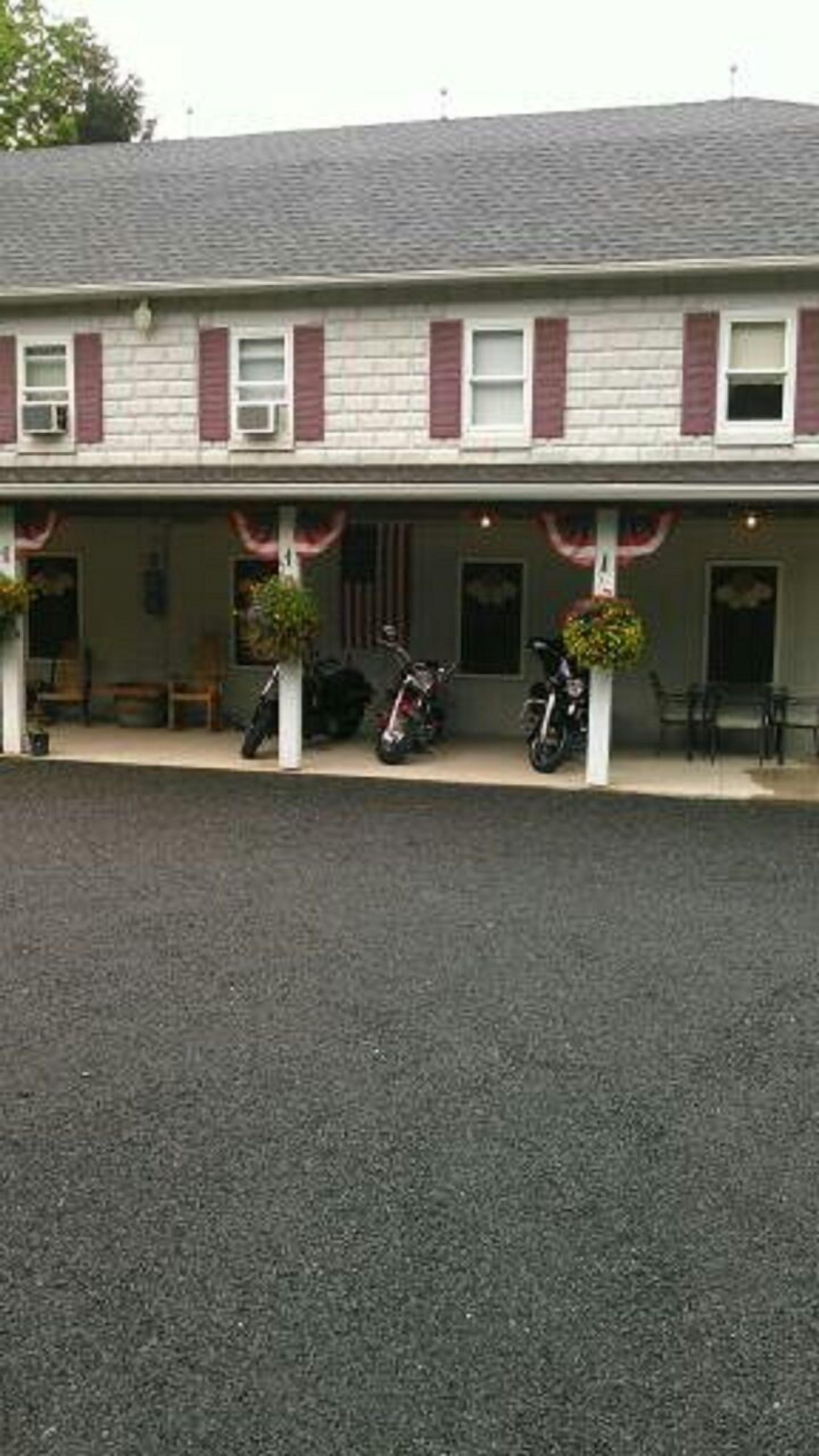 A two-story building with a covered porch, two motorcycles parked outside, and a bench on the porch.