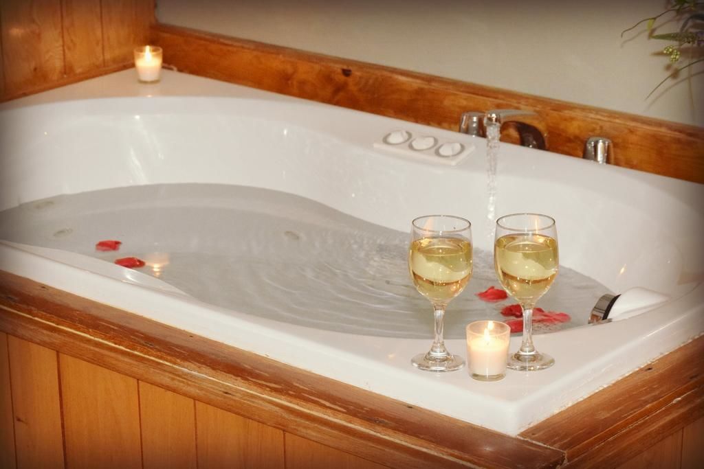 Une baignoire, deux verres de vin blanc, une bougie et des pétales de rose.