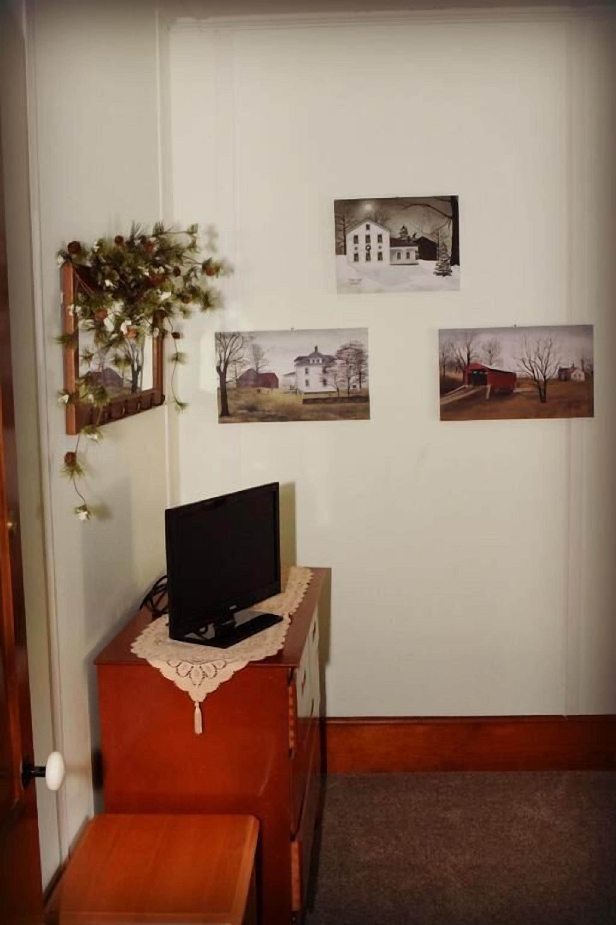 A room with a wooden desk, a television, and three framed pictures on the wall.