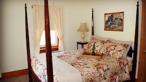 A four-poster bed with floral bedding, a bedside table with a lamp, and a framed landscape painting on the wall. - Beagle's Bed & Breakfast (Paxinos)