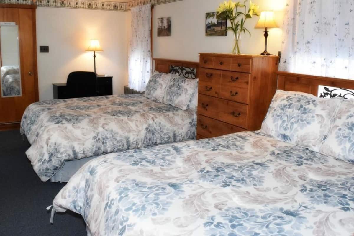 Une chambre d’hôtel avec deux lits, une commode en bois, un bureau et un miroir.