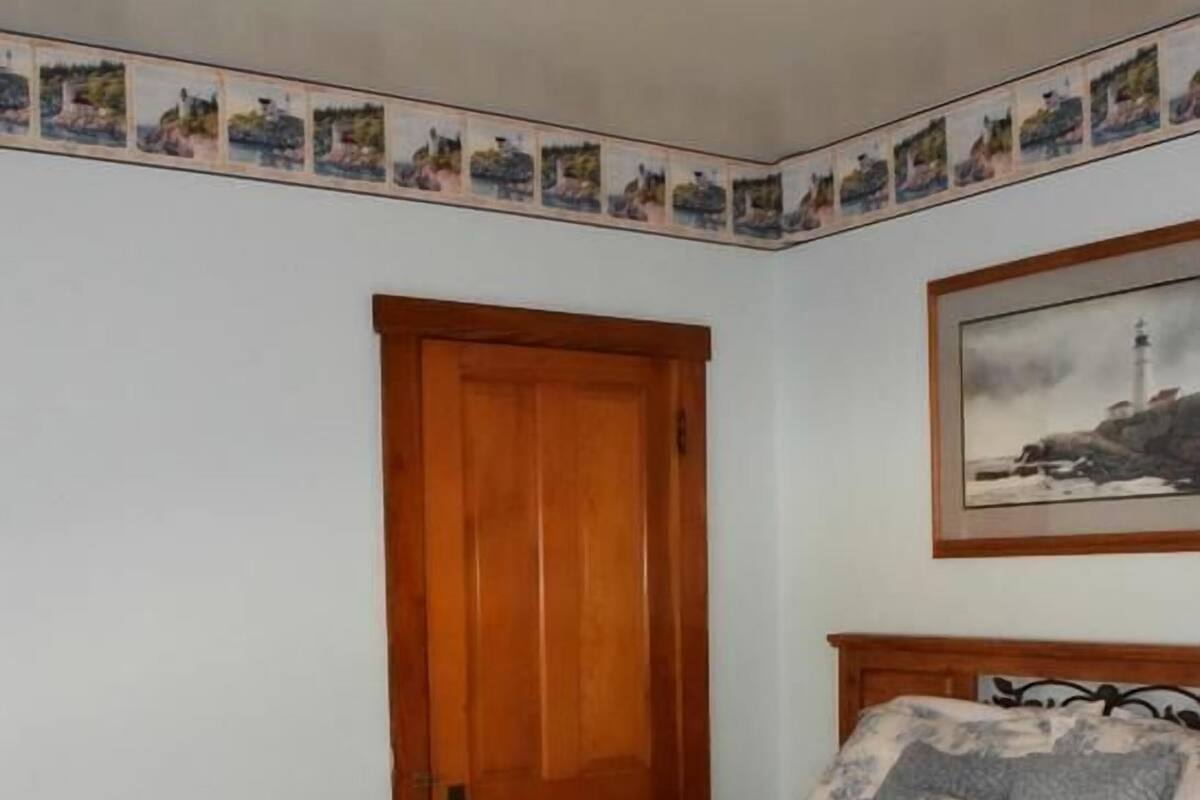Une chambre avec une porte en bois, un lit recouvert d’une courtepointe à motifs floraux et un tableau encadré accroché au mur.
