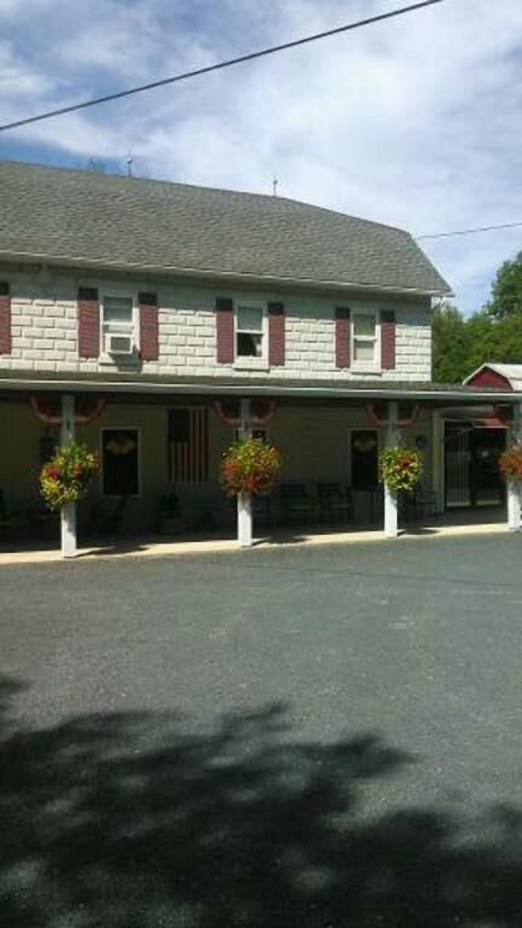 A two-story building with a flat roof and a porch with potted plants.