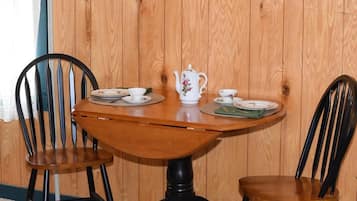 A wooden table with a white teapot and matching cups, flanked by two black chairs.