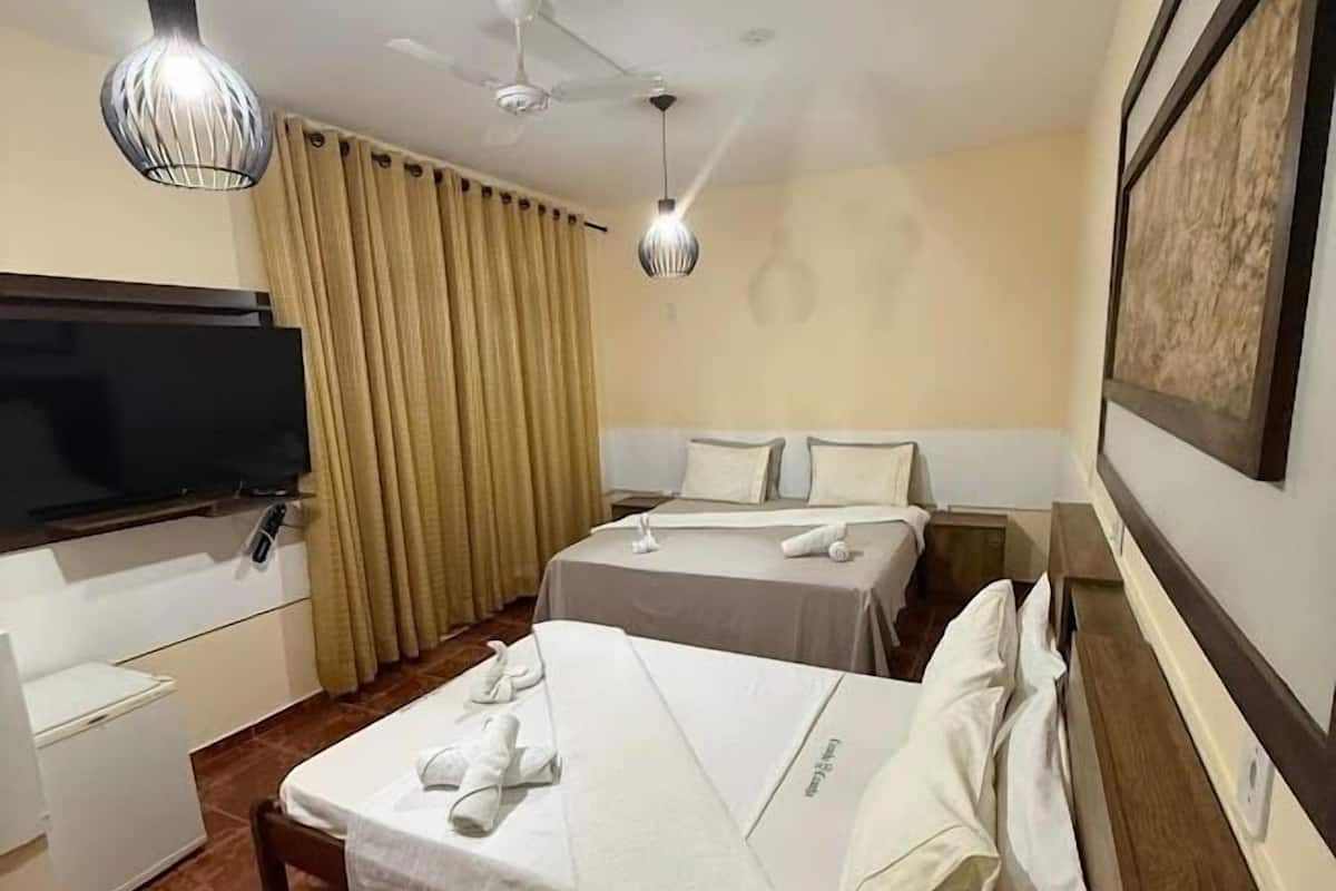 A hotel room with two beds, a TV, a desk, and a ceiling fan.