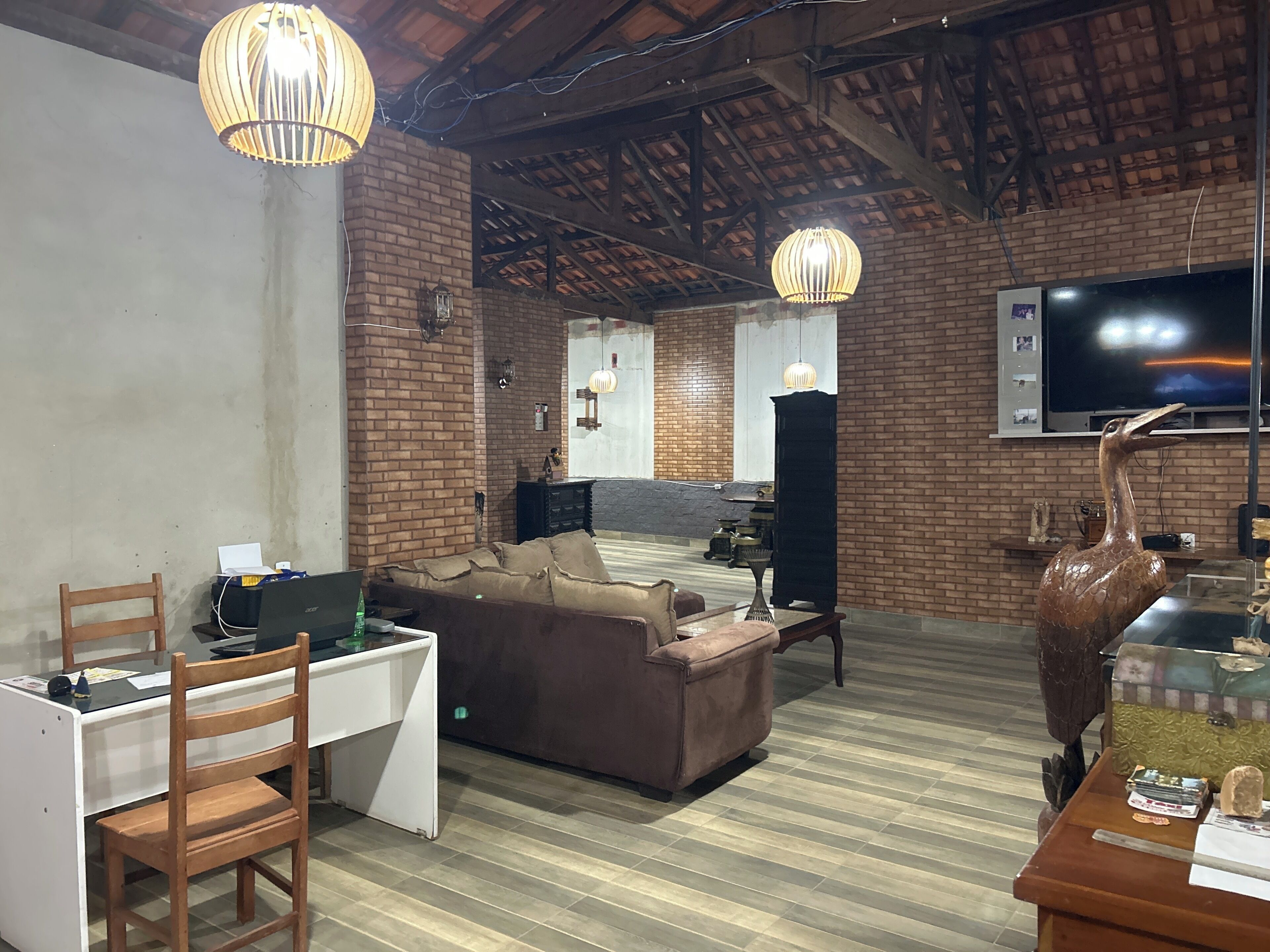 A room with a brick wall, a flat-screen TV, a sofa, a desk with a chair, and a wooden table.