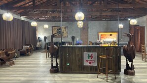 Un área de recepción con mostrador de madera, dos estatuas decorativas de aves, un letrero que indica recepción y una pared de ladrillo con un cuadro enmarcado.