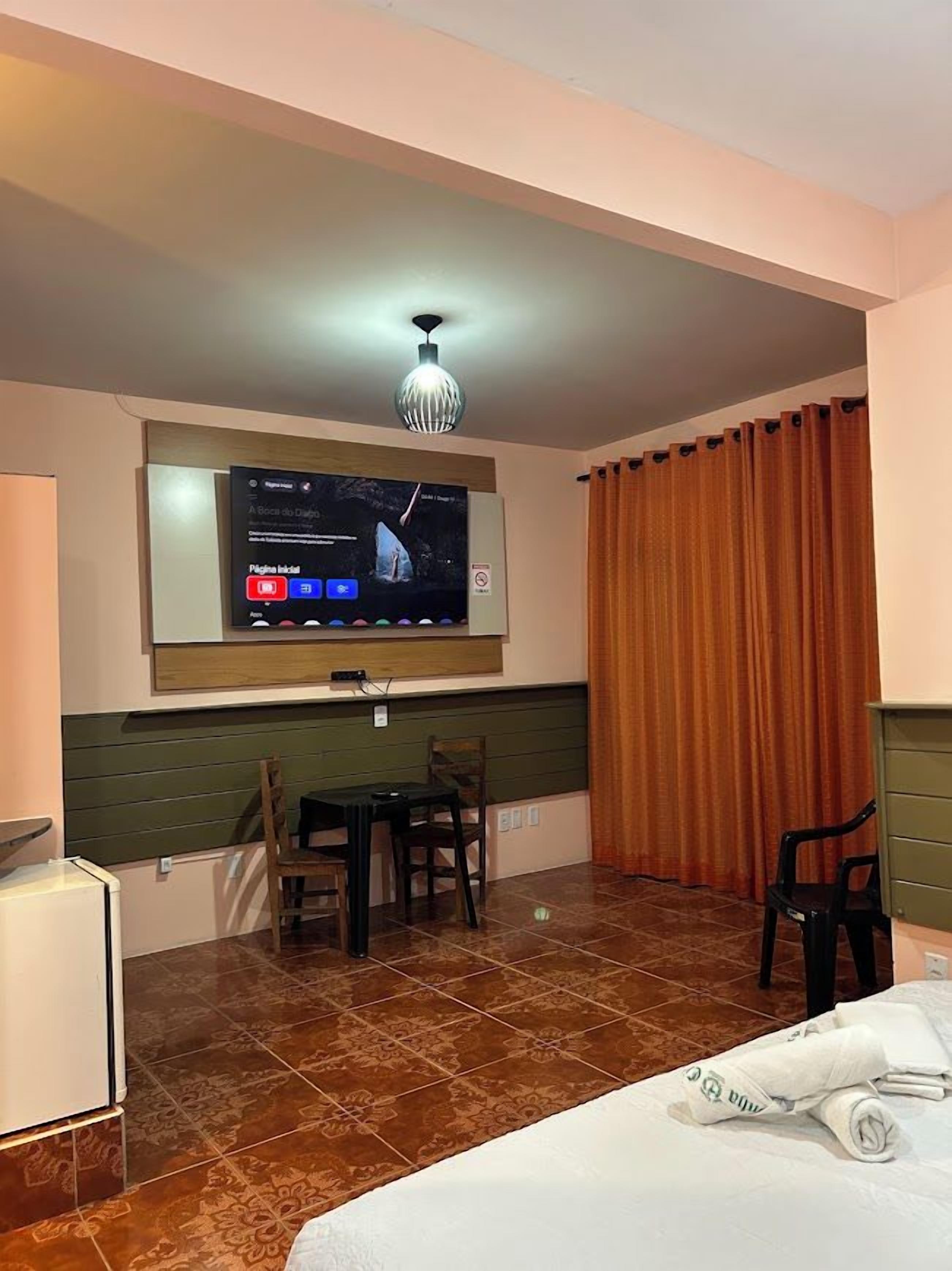 A hotel room with a bed, a TV mounted on the wall, a small table with chairs, and a window with curtains.