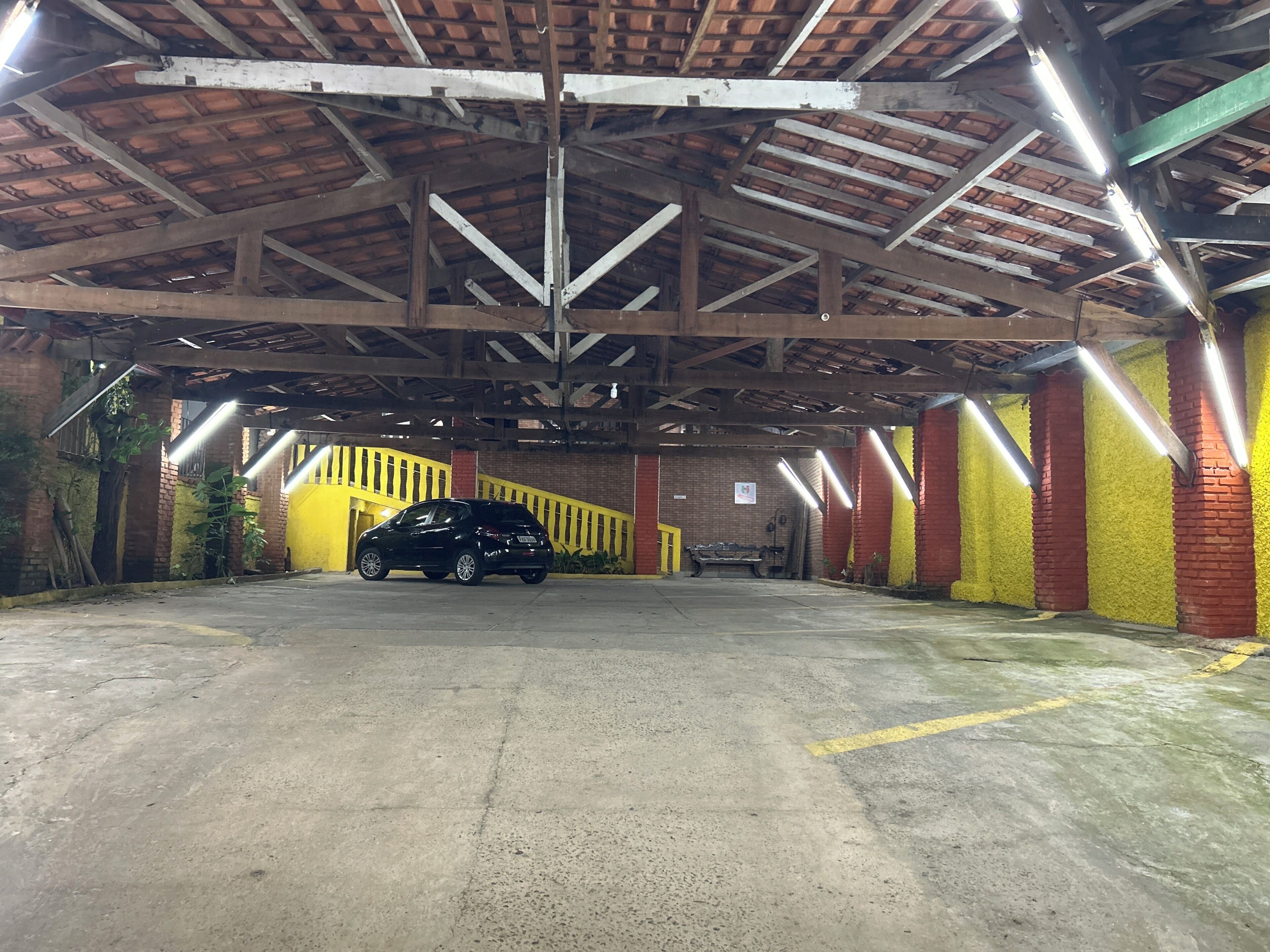 A parking garage with a black car parked in the center, concrete floor, and yellow and red brick walls.