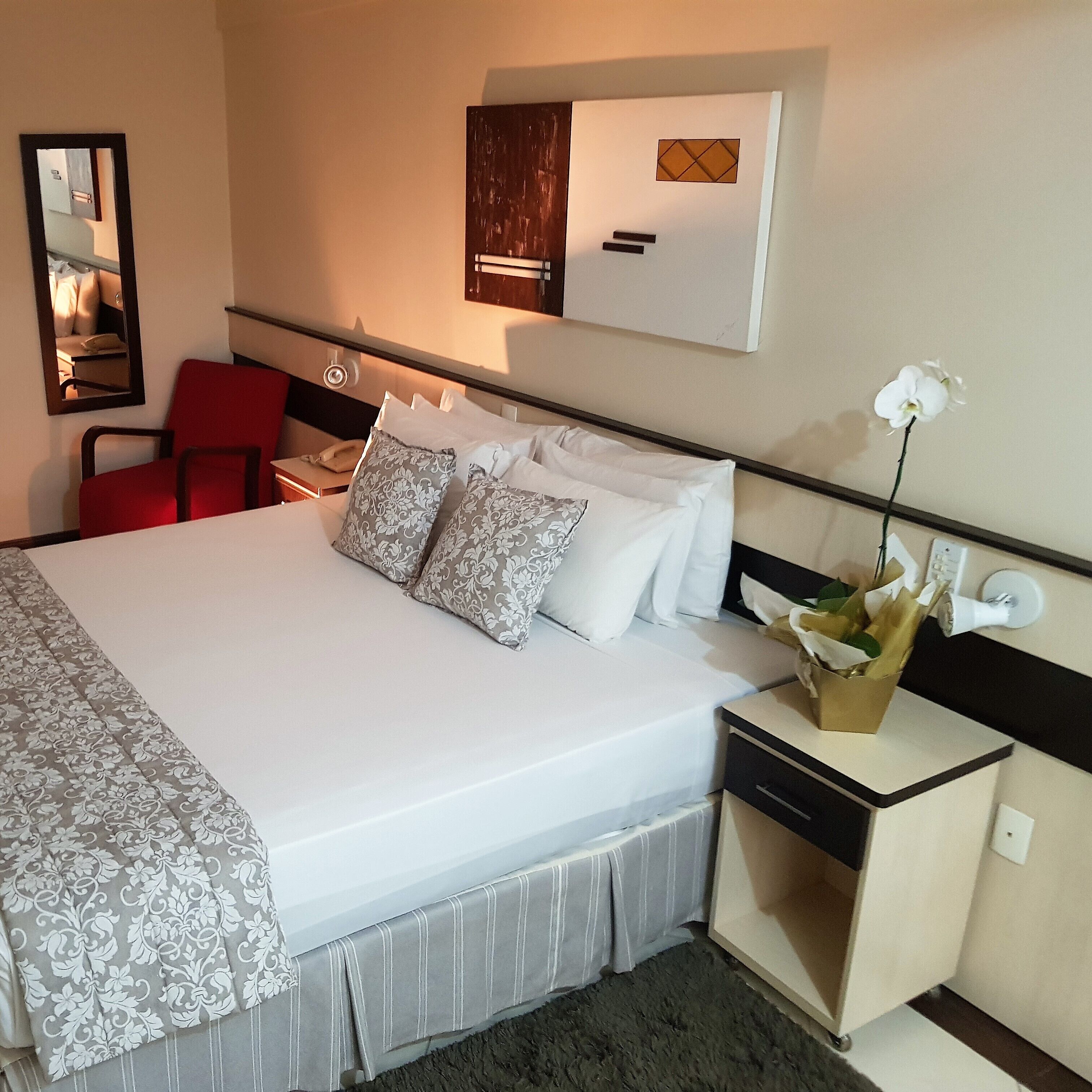 A hotel room with a bed, a desk, a chair, a mirror, and a wall-mounted TV.