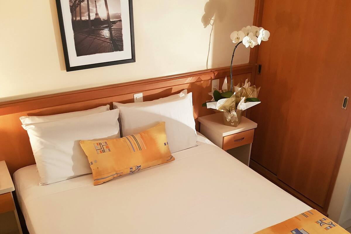A hotel room with a bed, pillows, a nightstand, a framed picture on the wall, and a door.