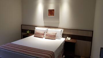 A modern hotel room with a neatly made bed, a bedside table with a lamp, and a small plant.