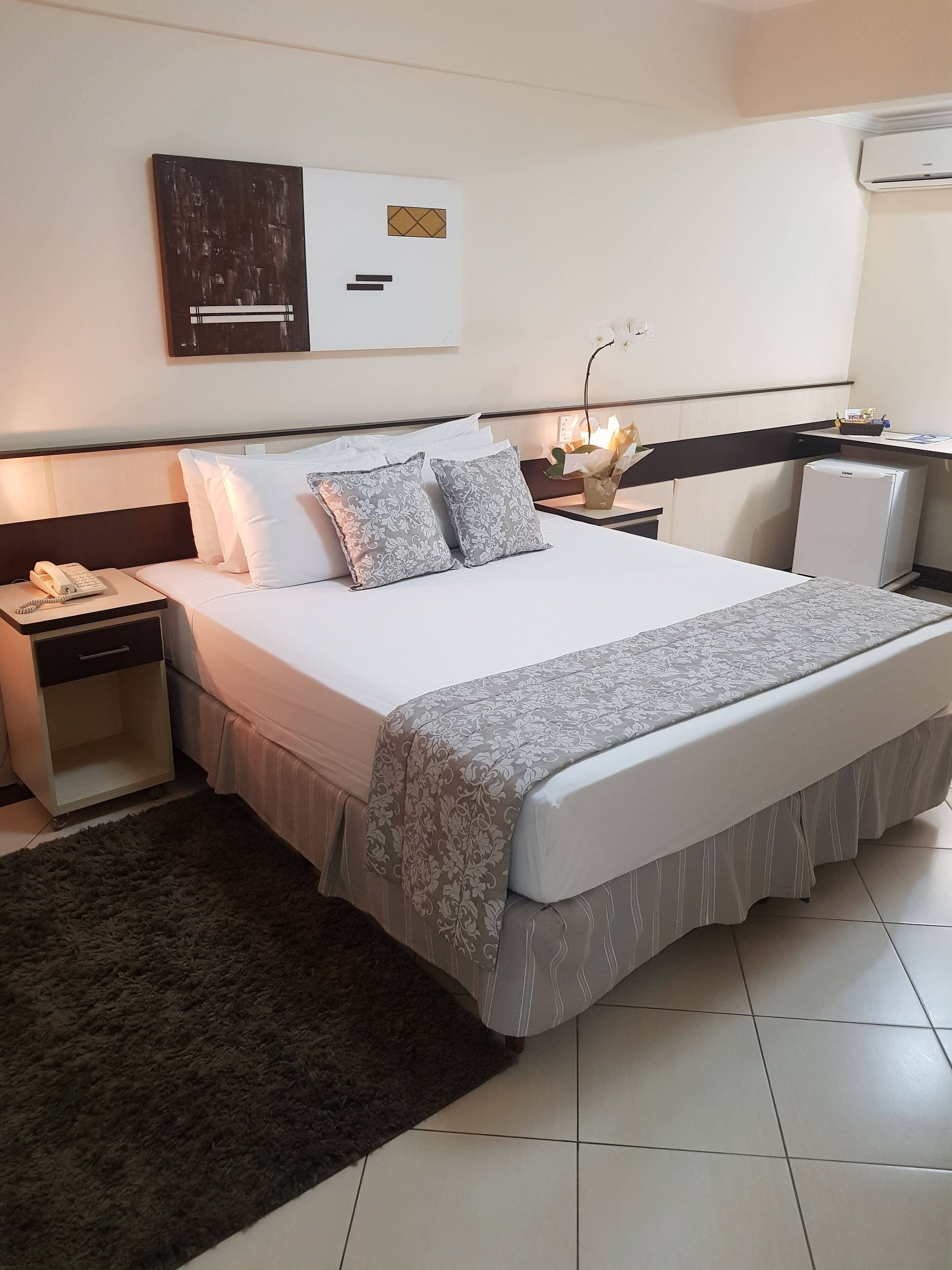 Ett välordnat hotellrum med en stor säng, sängbord, ett skrivbord och ett litet kylskåp.