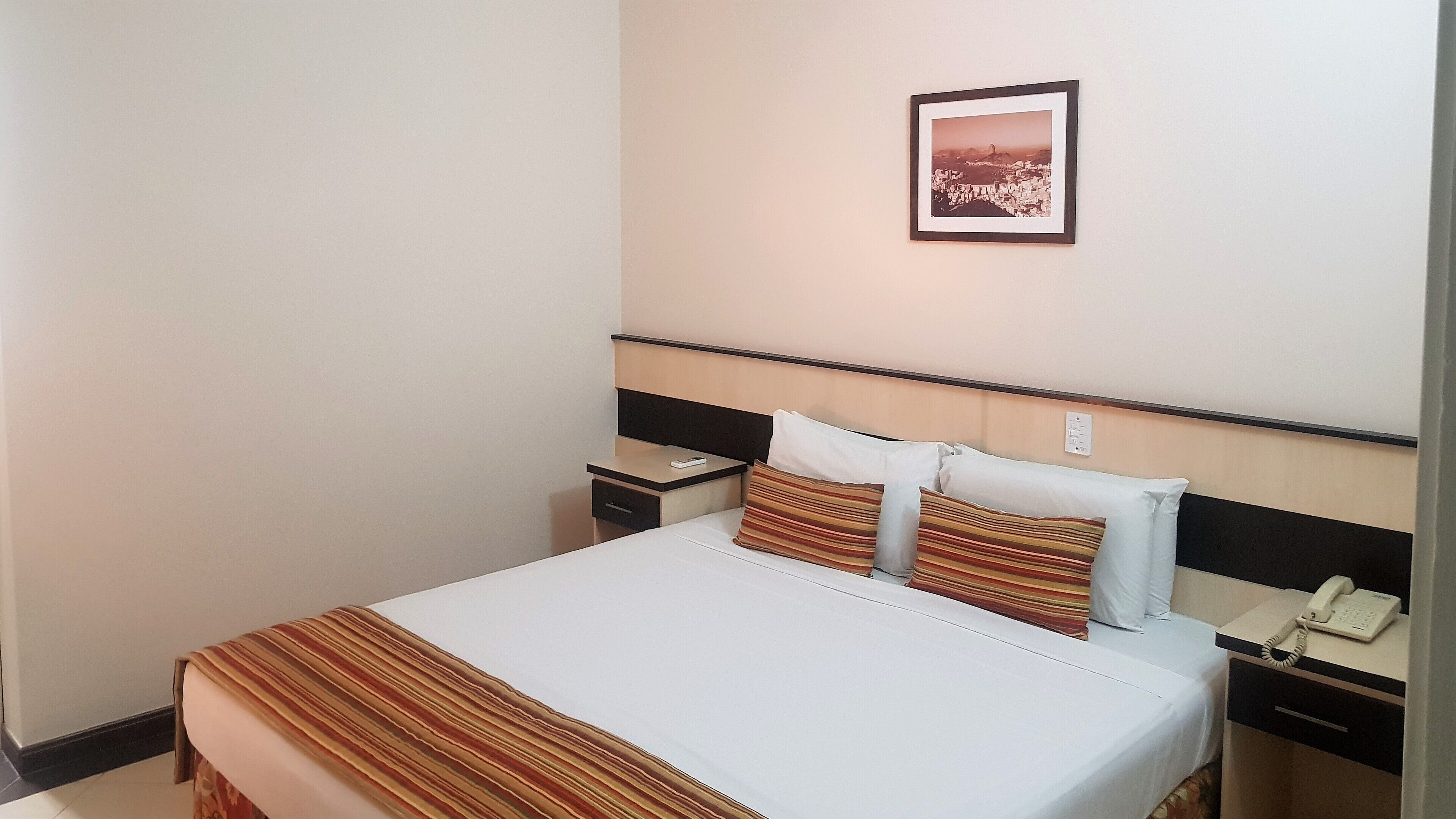 A hotel room with a bed, bedside tables, a telephone, and a framed picture on the wall.